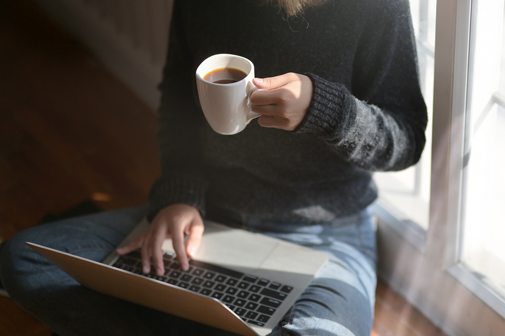 Homeoffice. Eine Person trinkt einen Kaffee / Tee und arbeitet am Laptop.