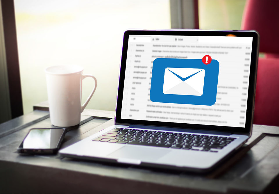 Ein Laptop steht auf einem Tisch, zu sehen ist eine E-Mail mit einem Warnsymbol, welches sich um eine Phishing-Mail handelt