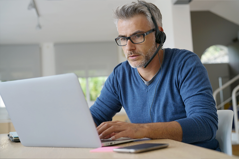 Ein Mann, der an einem Laptop sitzt und ein Headset trägt.